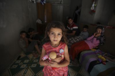 A small child holding a toy with her family sitting in the background