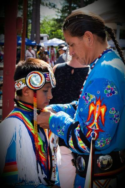 Native american man adjusting a young boy's ceremonial outfit