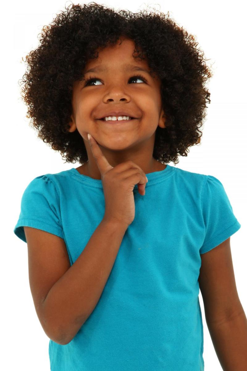 A young Black child smiles while looking upward with her finger on her chin.