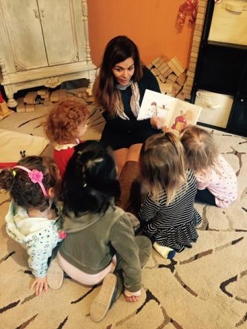 A photo of Anna Martinez sitting on the ground, reading to a group of young children