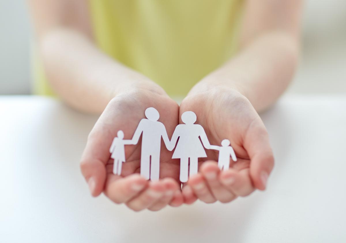 hands holding a paper cut-out of a family