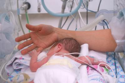 A newborn baby lies down at the hospital, with an adult's hand reaching out to touch it.