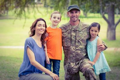 A family of four, including a father in military clothing, in a green field.