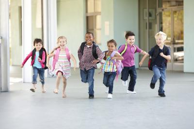 Young children wearing backpacks, running in a hallway.