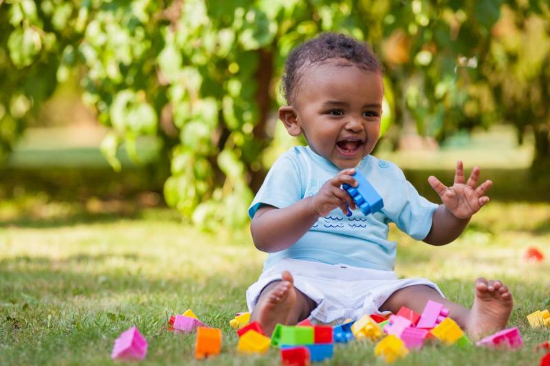A smiling baby playing with Lego's in the backyard.