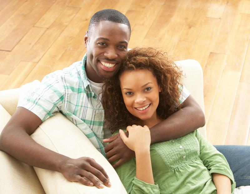 A couple holds hands while smiling and sitting on a couch. 
