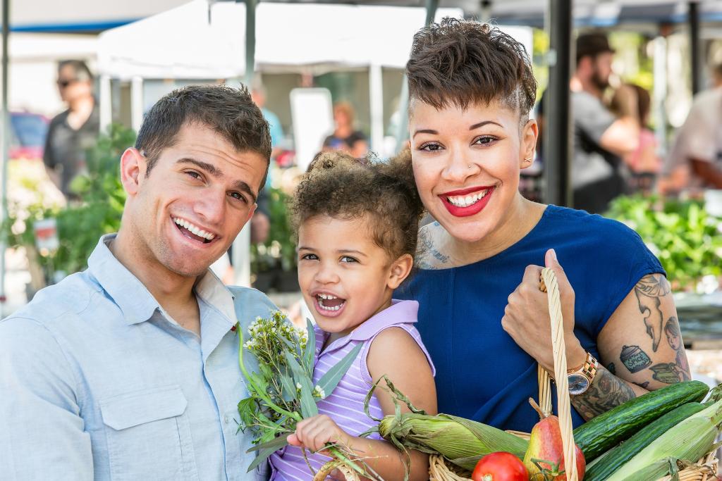 A biracial mom and dad holding their child at a market 