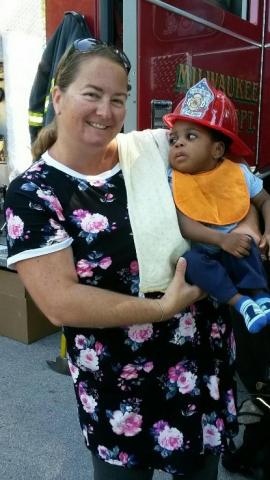 A photo of Wendy Lopez holding a young boy wearing a firehat